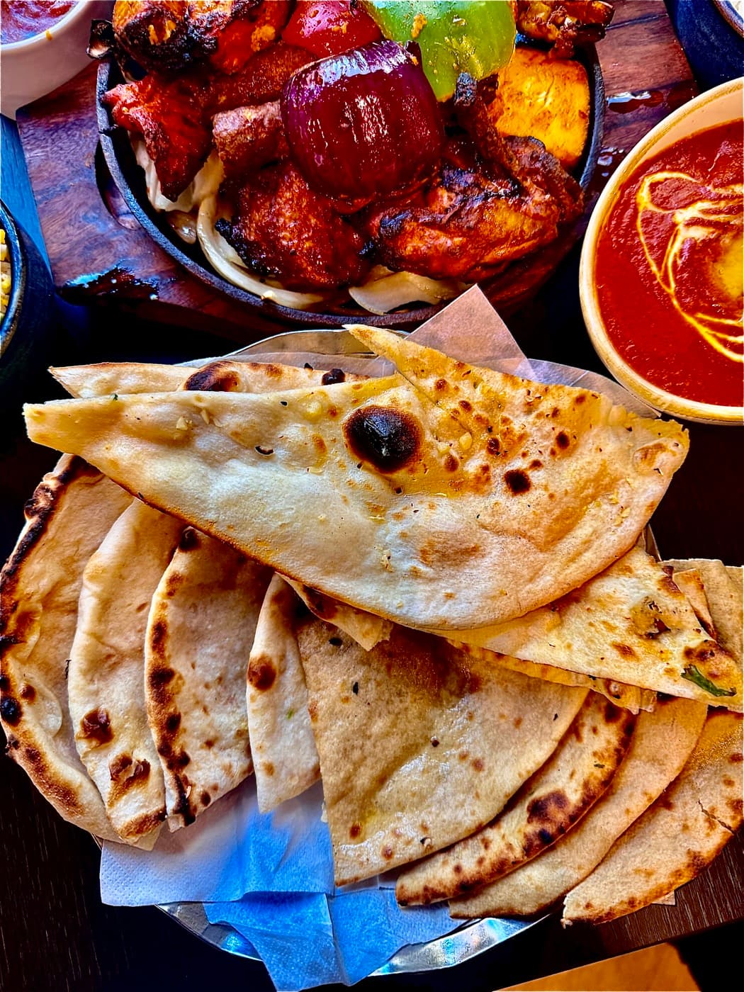 A basket of freshly made breads at Tempering (tandoori roti, garlic naan and peshwari naan) beside a tandoori grill and curry